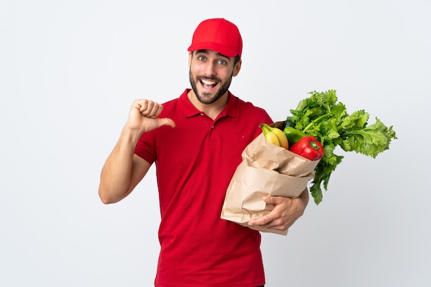 Jeune homme à la barbe tenant un sac plein de légumes isolé sur un mur blanc fier et satisfait de lui-même