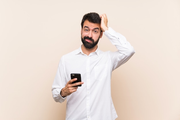 Jeune Homme à La Barbe Tenant Un Téléphone Portable Avec Une Expression De Frustration Et De Non Compréhension