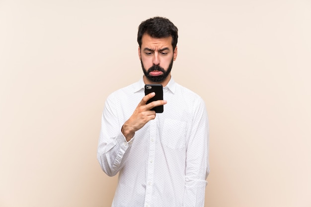 Jeune Homme à La Barbe Tenant Un Téléphone Portable Avec Une Expression Triste Et Déprimée