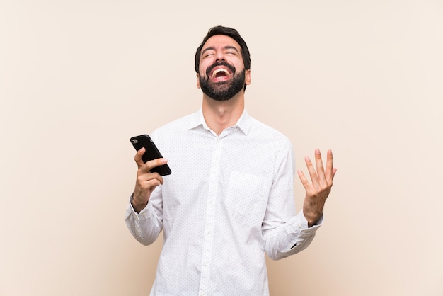 Jeune homme à la barbe tenant un téléphone portable souriant beaucoup