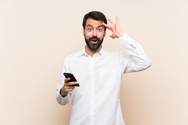 Jeune homme à la barbe tenant un téléphone portable vient de réaliser quelque chose et a l'intention de la solution