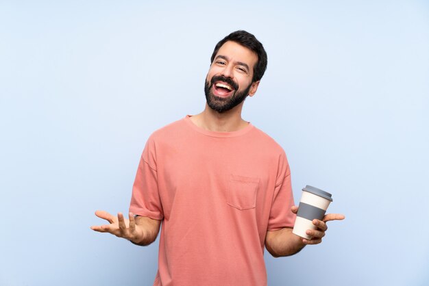 Jeune homme, à, barbe, tenue, a emporter, café, sur, isolé, mur bleu, sourire