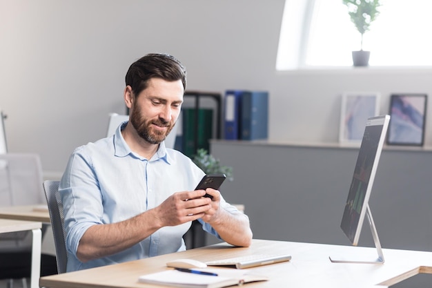Jeune homme avec une barbe travailleur indépendant manager parlant sur un téléphone portable dans le bureau assis à un bureau d'ordinateur parlant en agitant