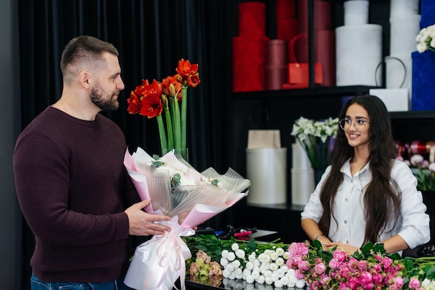 Un jeune homme barbu achète un beau bouquet de fleurs pour les vacances d'une fille dans un fleuriste confortable Fleuriste et confection de bouquets dans un fleuriste Petite entreprise