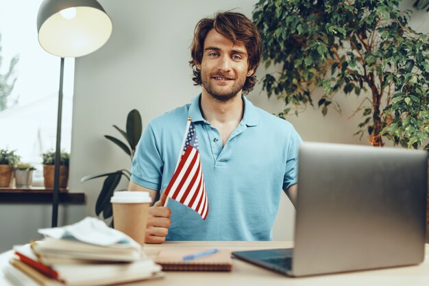 Jeune homme barbu assis à table avec ordinateur portable et drapeau américain