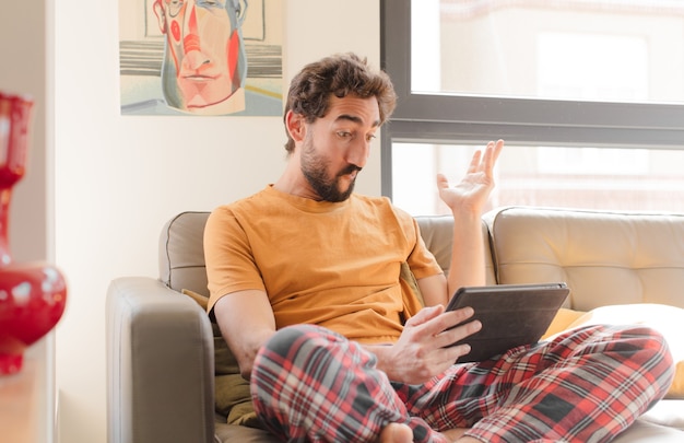 Jeune homme barbu sur un canapé avec une tablette à écran tactile