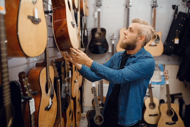 Jeune homme barbu en choisissant une guitare dans un magasin de musique