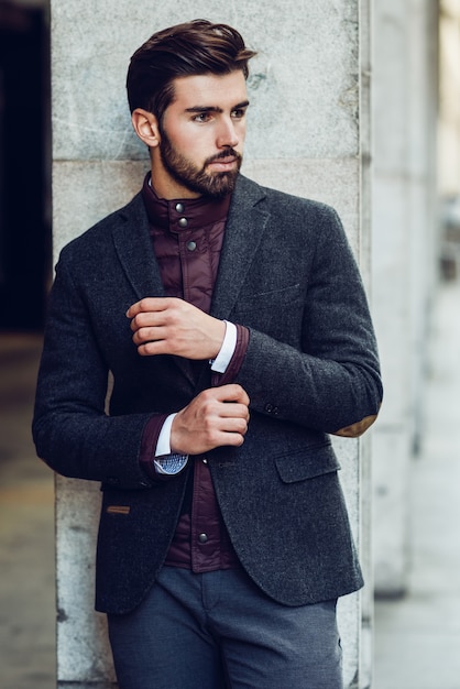 Jeune homme barbu en contexte urbain portant costume élégant britannique dans la rue.