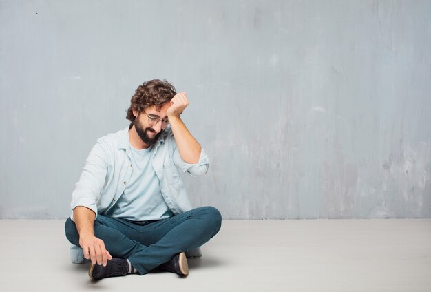 Jeune homme barbu cool assis sur le sol. fond de mur de grunge