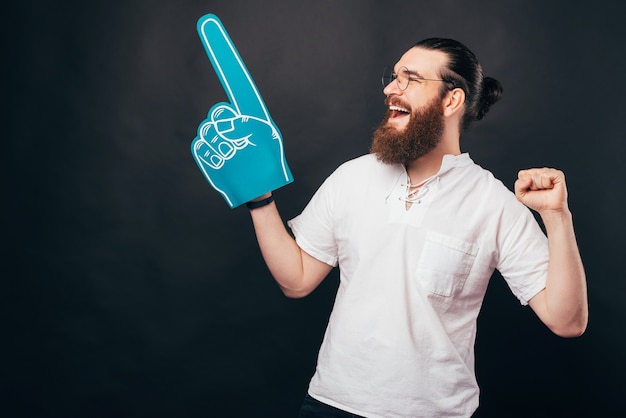 Un jeune homme barbu excité tient un gant de ventilateur bleu regardant et souriant