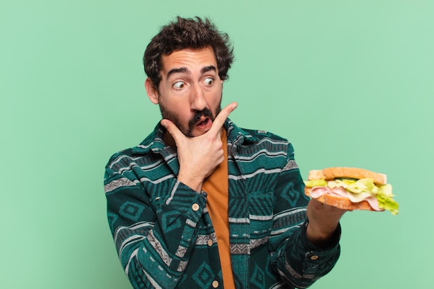 Jeune homme barbu fou doutant ou incertain d'expression et tenant un sandwich