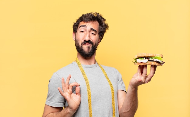 Jeune homme barbu fou avec une expression heureuse et tenant un sandwich