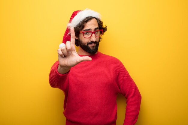 Jeune homme barbu fou portant des lunettes rouges et un chapeau de père Noël