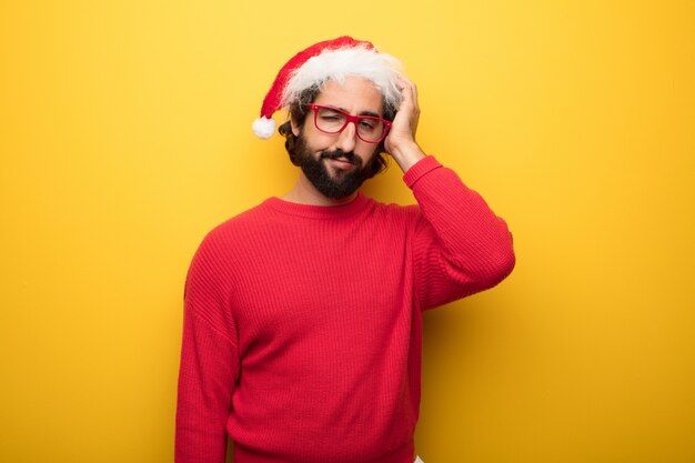 Jeune homme barbu fou portant des lunettes rouges et un chapeau de père Noël