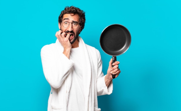 Jeune homme barbu fou portant un peignoir de cuisine avec une casserole