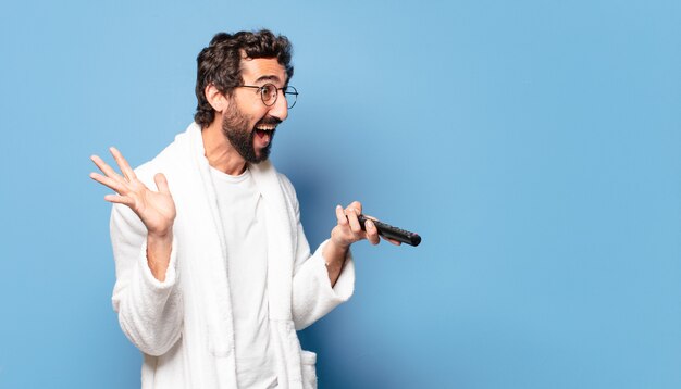 Jeune homme barbu fou portant un peignoir avec une télécommande