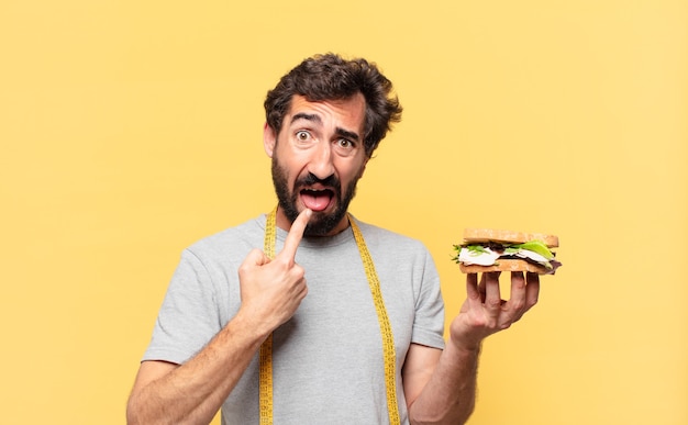 Jeune homme barbu fou suivant un régime d'expression en colère et tenant un sandwich