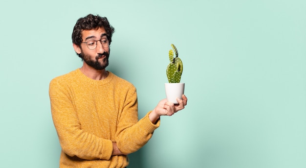 Jeune homme barbu fou tenant une plante d'intérieur de cactus