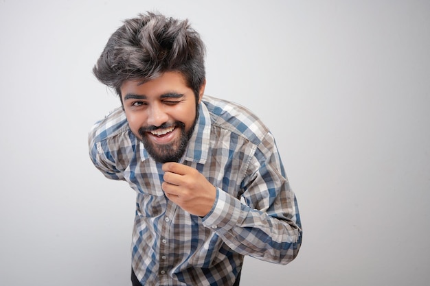 Jeune homme barbu hispanique portant une chemise à carreaux sur fond blanc avec une expression positive a un large sourire intéressé