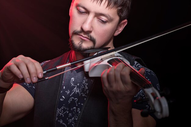 Jeune homme barbu jouant un violon électrique blanc, isolé sur fond noir