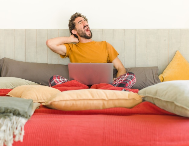 Jeune homme barbu sur un lit avec un ordinateur portable