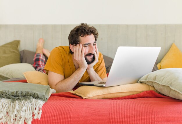 Jeune homme barbu sur un lit avec un ordinateur portable