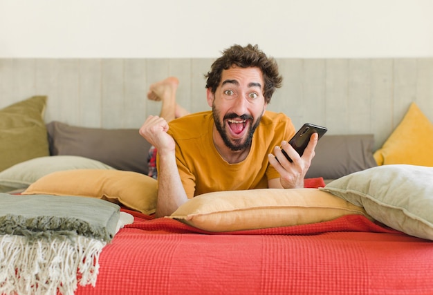 Jeune homme barbu sur un lit avec son téléphone portable