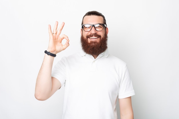 Jeune homme barbu montre un geste ok sur fond blanc.