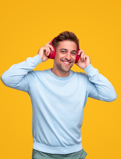 Jeune homme barbu optimiste dans des vêtements décontractés et des écouteurs sans fil s'amusant et profitant de la bonne musique sur fond jaune