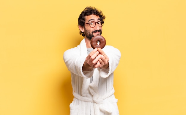 Jeune homme barbu portant un peignoir avec un beignet au chocolat