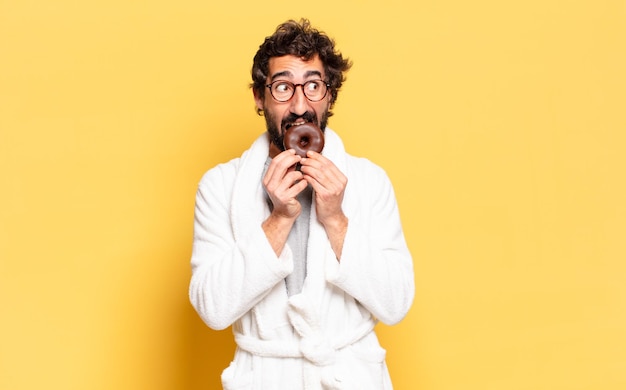 Jeune homme barbu portant un peignoir avec un beignet au chocolat