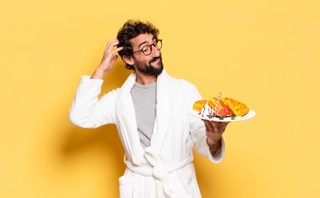 Jeune homme barbu portant un peignoir et prenant son petit déjeuner