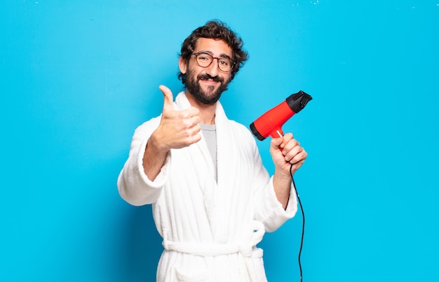 Jeune homme barbu portant un peignoir avec un sèche-cheveux