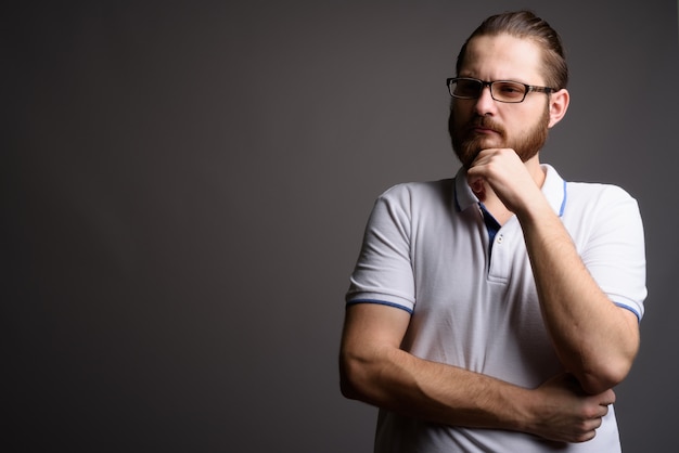 Jeune homme barbu portant un polo blanc contre un mur gris