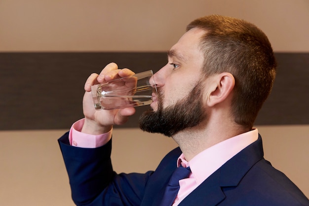 Un jeune homme barbu qui boit de l&#39;eau dans un verre.