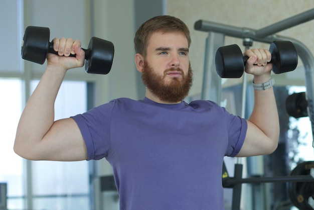 Jeune homme barbu s'entraînant dans la salle de gym avec des haltères