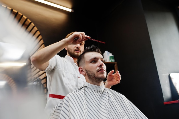 Jeune homme barbu se coupe les cheveux par le coiffeur alors qu'il était assis sur une chaise au salon de coiffure