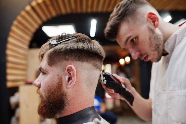 Jeune homme barbu se coupe les cheveux par le coiffeur assis sur une chaise au salon de coiffure. Âme de coiffeur.