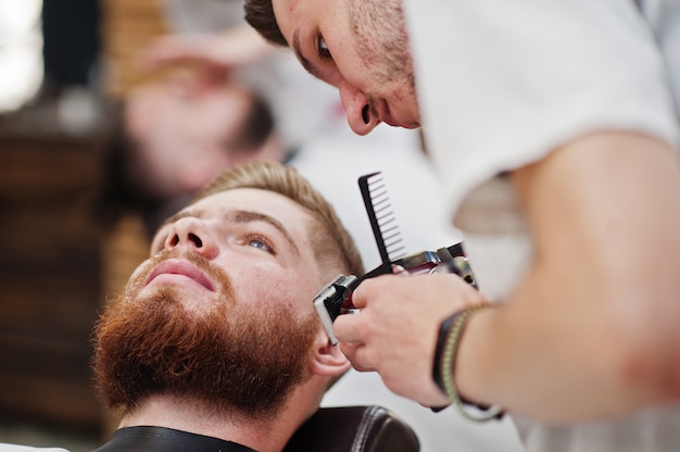 Jeune homme barbu se coupe les cheveux par le coiffeur assis sur une chaise au salon de coiffure. Âme de coiffeur.