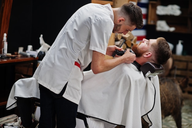 Jeune homme barbu se coupe les cheveux par le coiffeur assis sur une chaise au salon de coiffure. Âme de coiffeur.