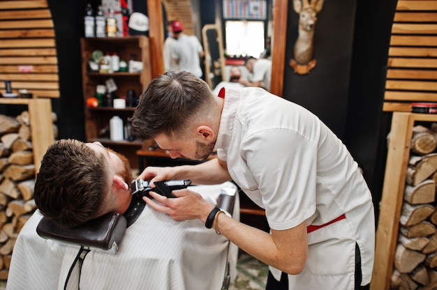 Jeune homme barbu se coupe les cheveux par le coiffeur assis sur une chaise au salon de coiffure. Âme de coiffeur.