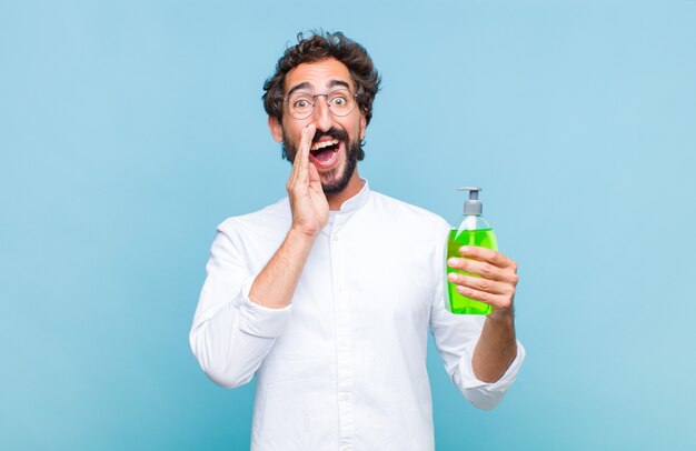 Jeune homme barbu se sentir heureux, excité et positif, donnant un grand cri avec les mains à côté de la bouche, appelant