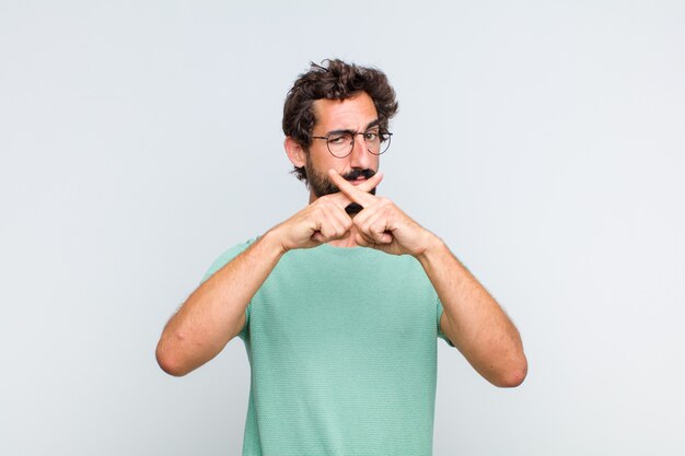 Jeune homme barbu à la sérieuse et mécontent avec les deux doigts croisés à l'avant en rejet