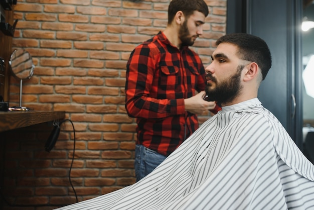 Jeune homme barbu sérieux se faisant couper les cheveux par un coiffeur. Thème du salon de coiffure