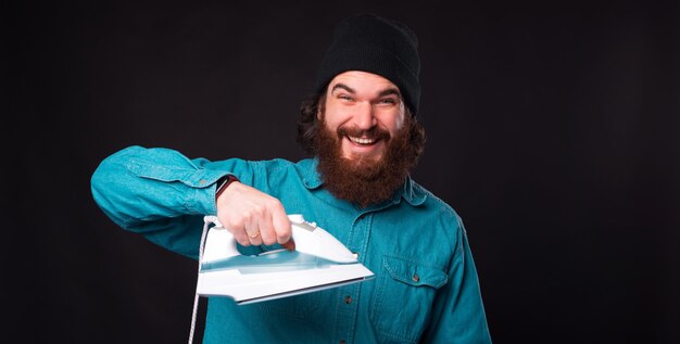 Jeune homme barbu souriant à la caméra tient un fer à repasser.