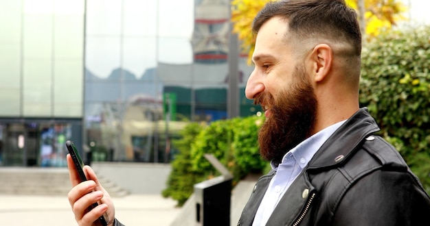 Jeune homme barbu souriant heureux de faire un appel vidéo à l'aide d'un smartphone en ville.
