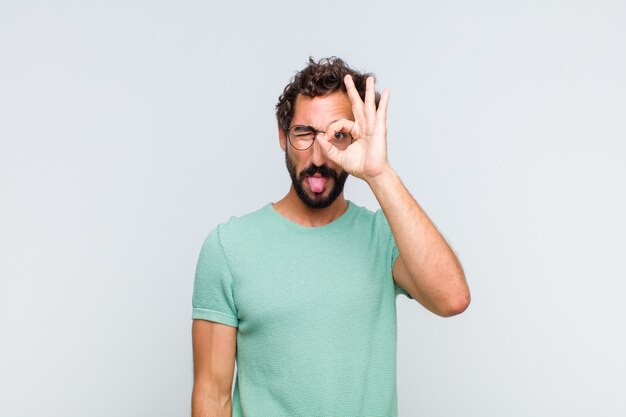 Jeune homme barbu souriant joyeusement avec grimace, plaisantant et regardant à travers le judas, espionnant les secrets