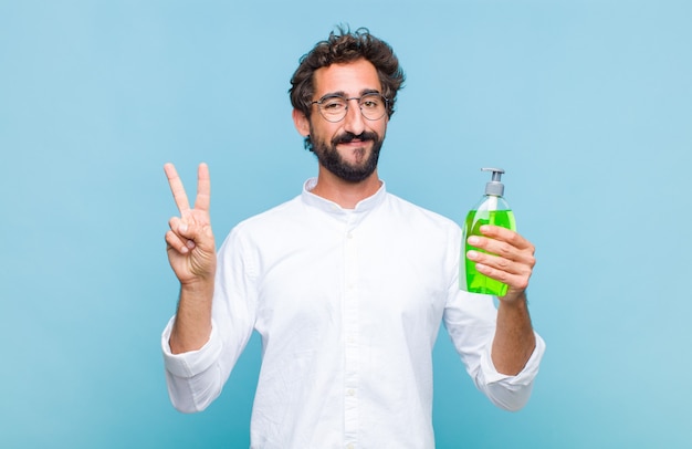 Jeune homme barbu souriant et à la sympathique, montrant le numéro deux ou seconde avec la main en avant, compte à rebours