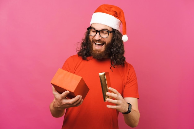 Un jeune homme barbu surpris ouvre le cadeau qu'il vient de recevoir pour Noël