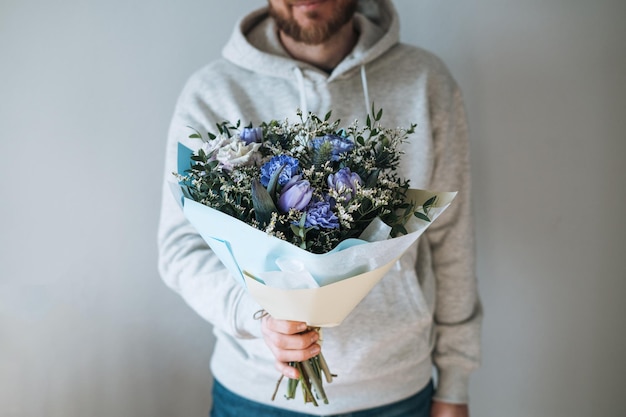 Jeune homme barbu en sweat à capuche gris avec bouqet de fleurs dans les mains sur fond gris